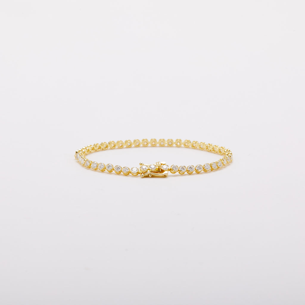 Gold-tone bracelet with a row of round clear stones, viewed at a low angle with the clasp at the front.