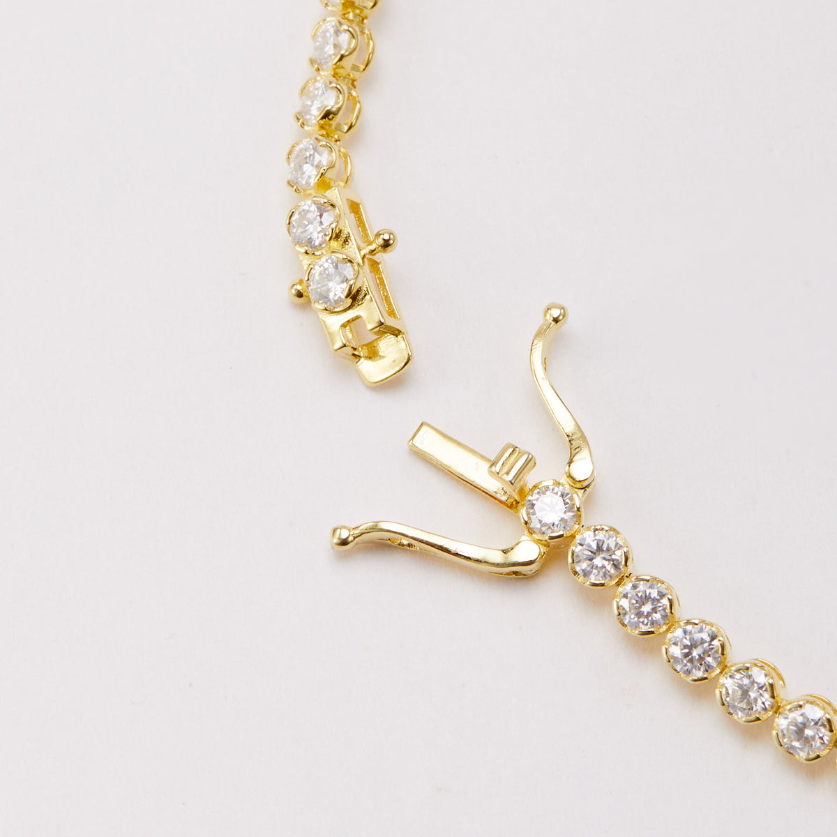 Close-up of a gold-tone bracelet with round clear stones and its clasp open, showing the tongue and two safety arms.