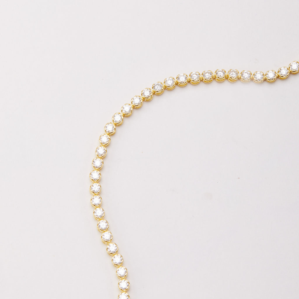 Close-up of a curved row of round clear stones in gold-tone bracelet settings on a light background.