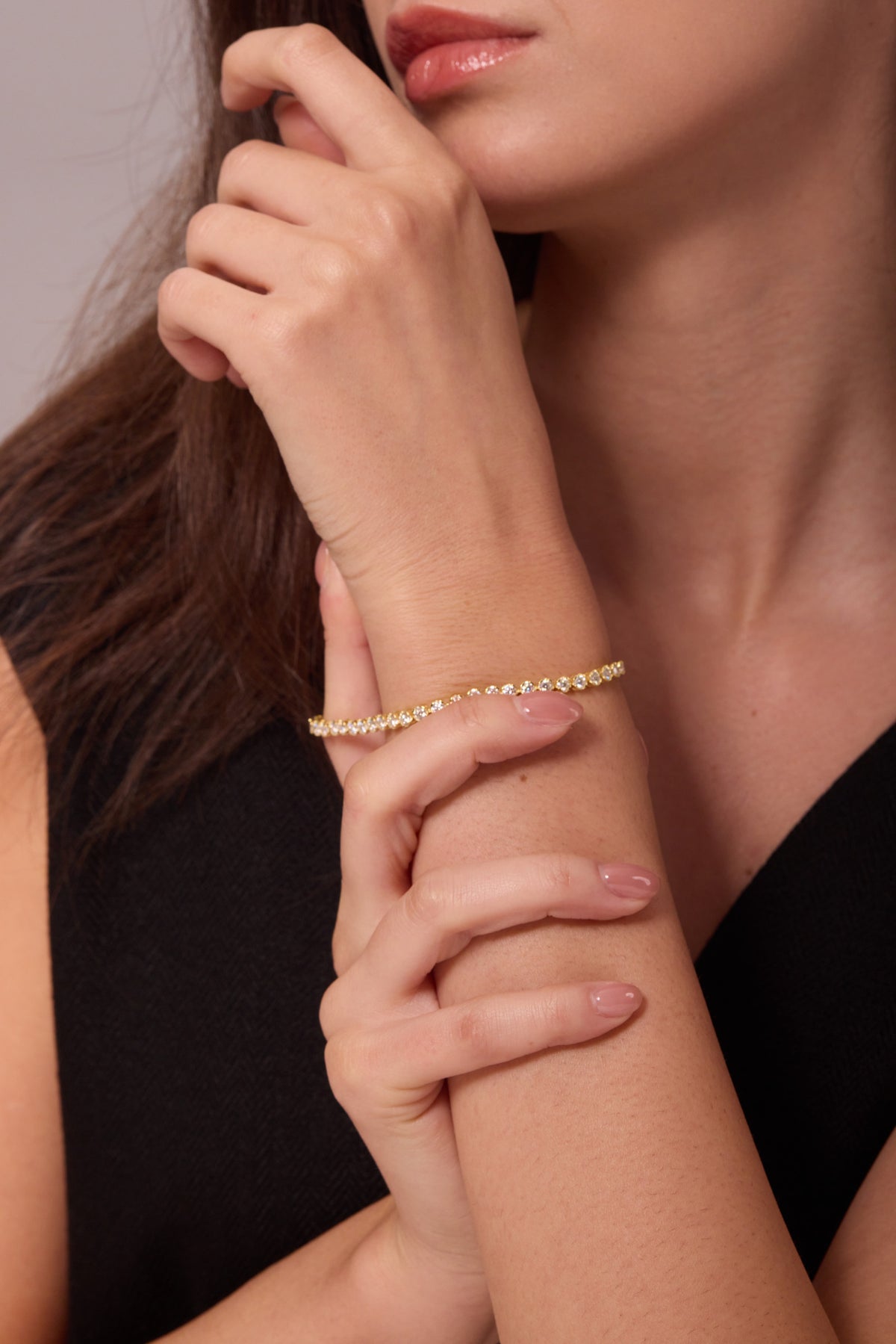 Gold-tone bracelet with clear stones on a raised wrist, with the other hand resting below it.
