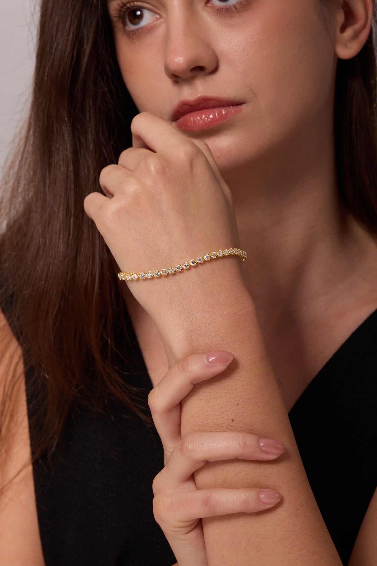 Gold-tone bracelet with round clear stones worn on a wrist raised near the chin.