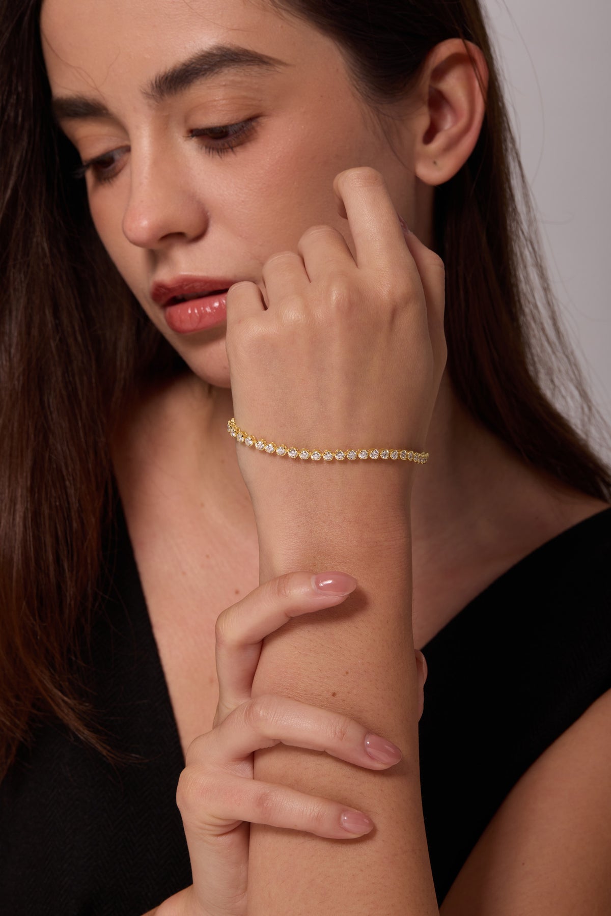 Gold-tone bracelet with round clear stones on a raised wrist beside the face.
