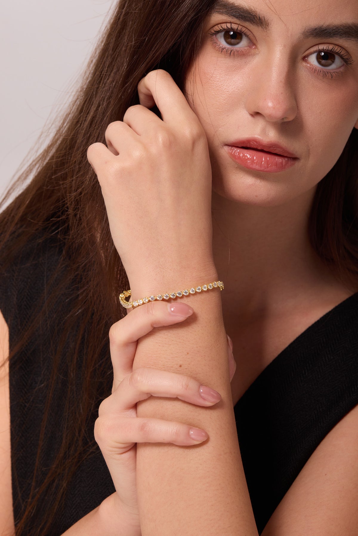 Gold-tone bracelet with round clear stones on a raised wrist, supported by the other hand.