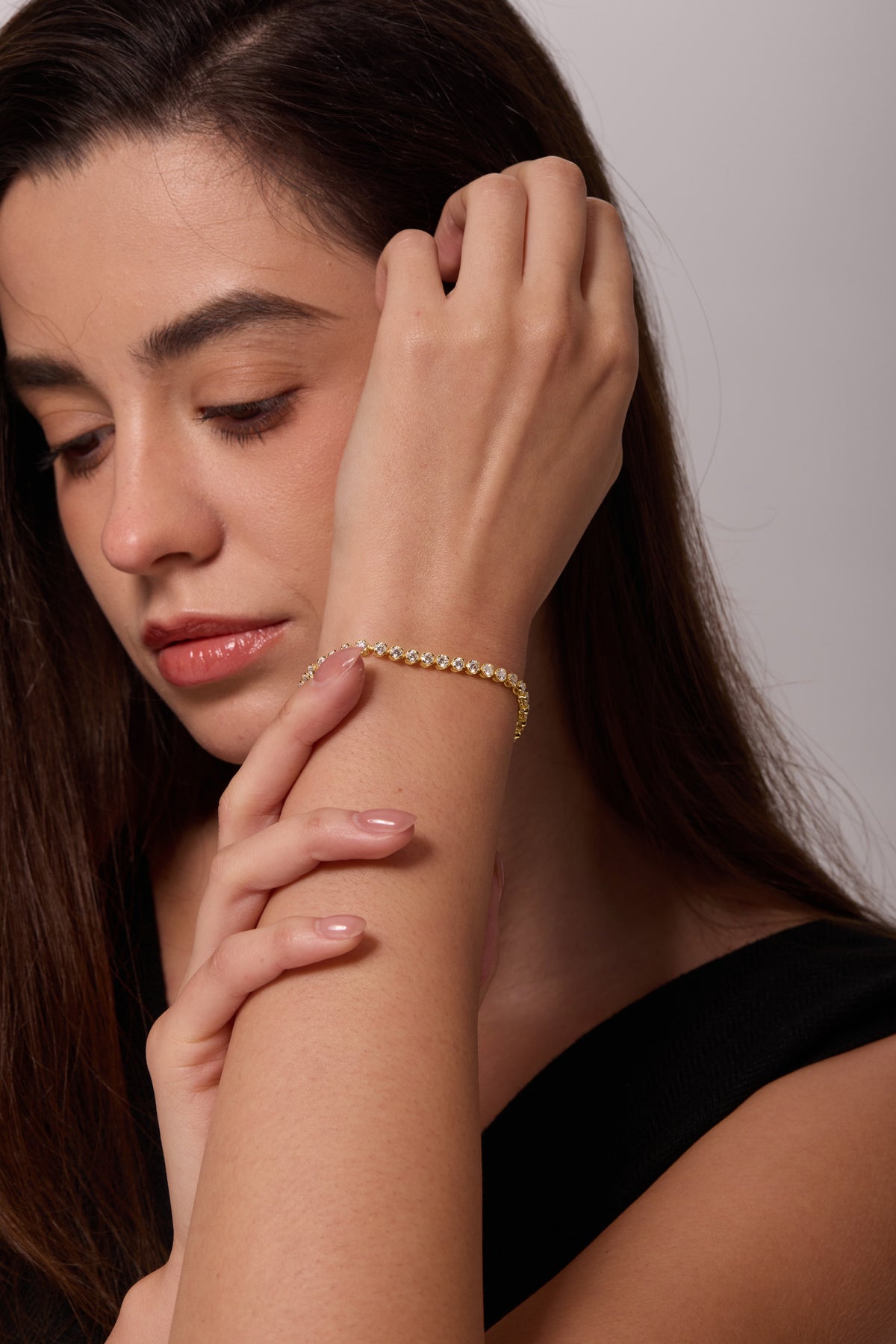 Gold-tone bracelet with round clear stones on a raised wrist, with a fingertip touching the bracelet.