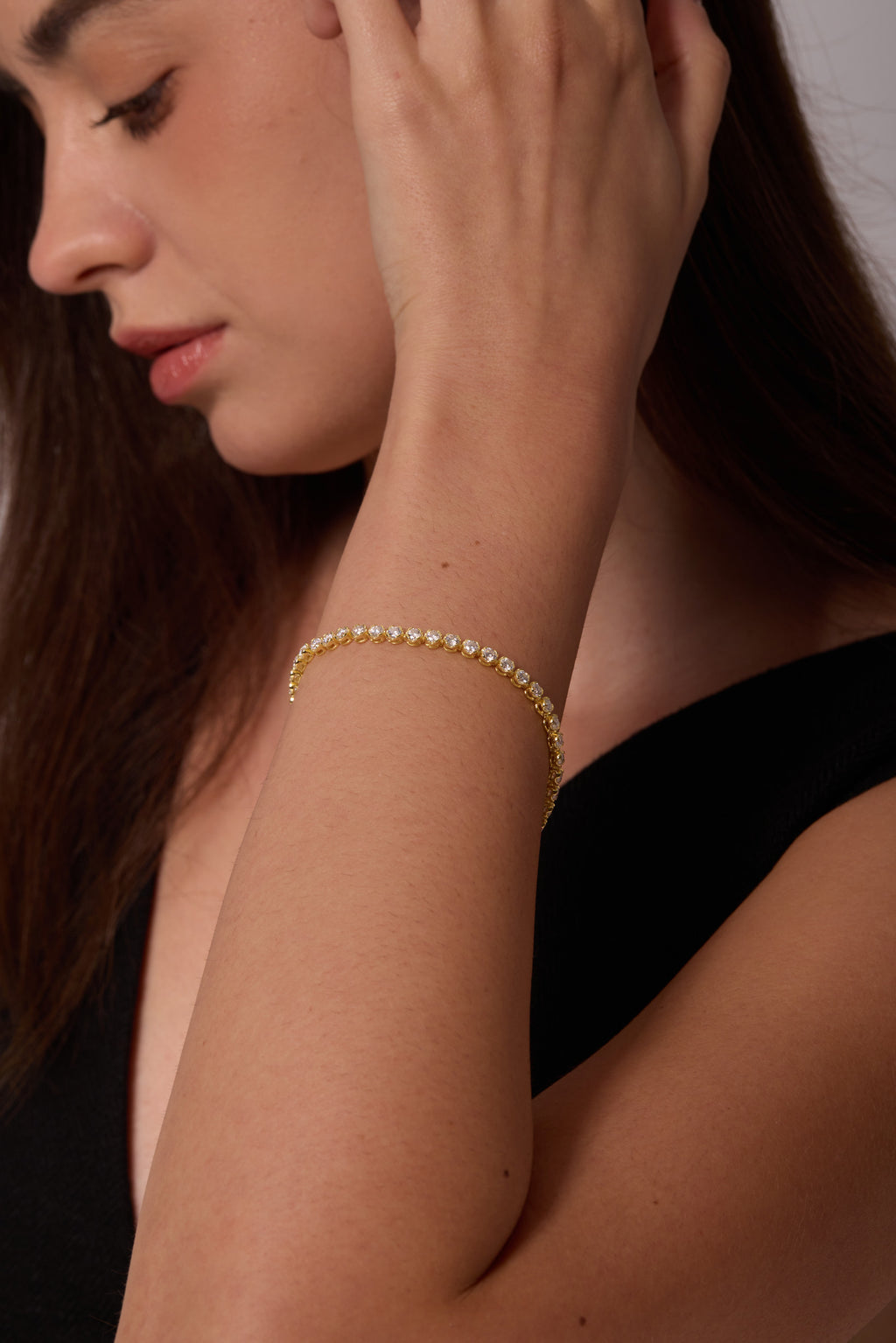 Gold-tone bracelet with round clear stones, worn on a wrist held beside the face.