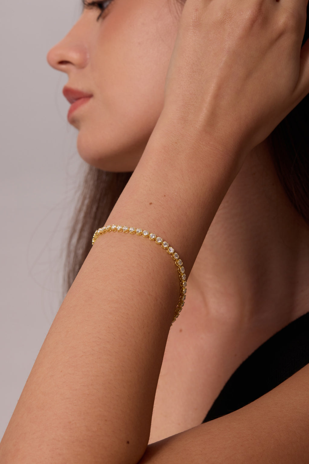 Side view of a gold-tone bracelet with round clear stones on a wrist raised beside the face.