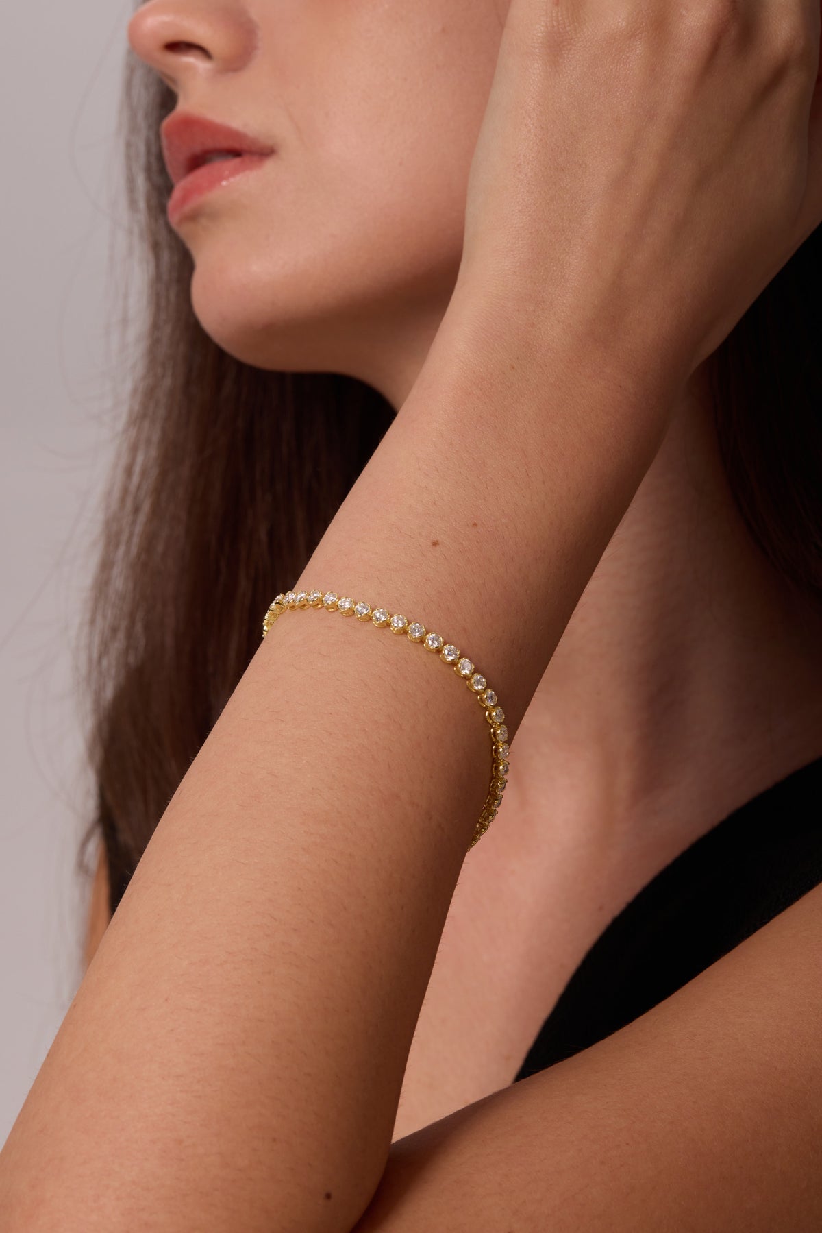 Gold-tone bracelet with round clear stones on an angled wrist raised beside the face.