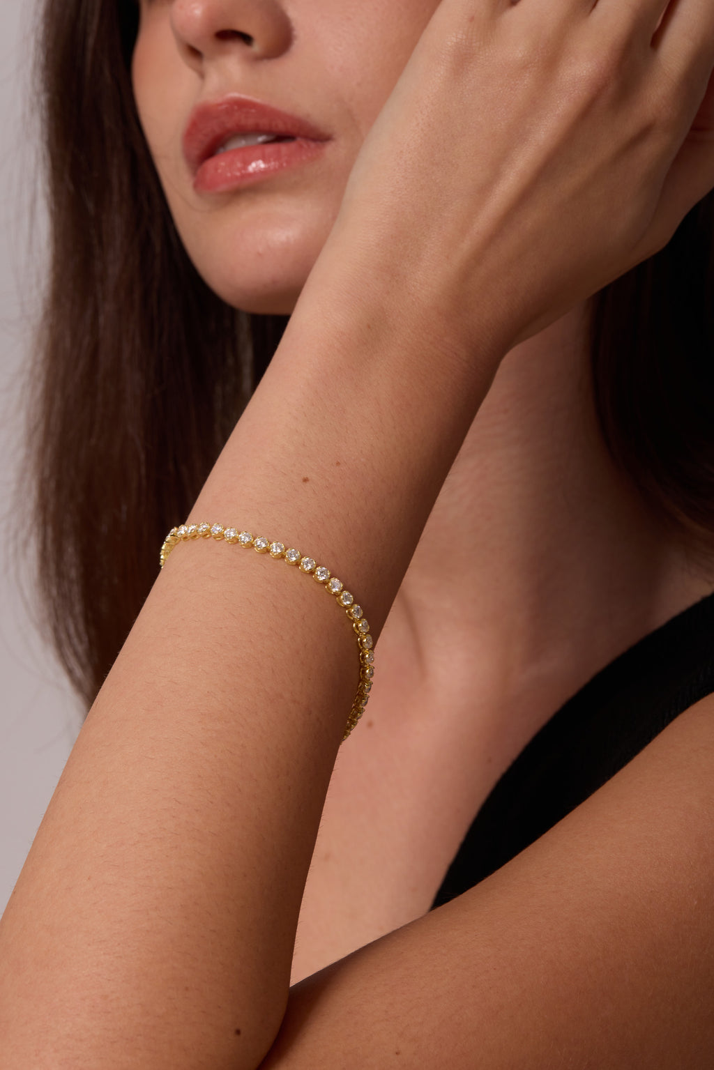 Close view of a gold-tone bracelet with round clear stones on a wrist raised beside the face.