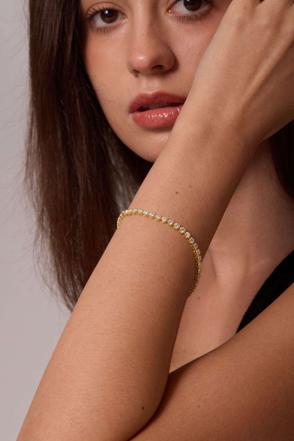 Gold-tone bracelet with a row of round clear stones, worn on a wrist angled across the face.