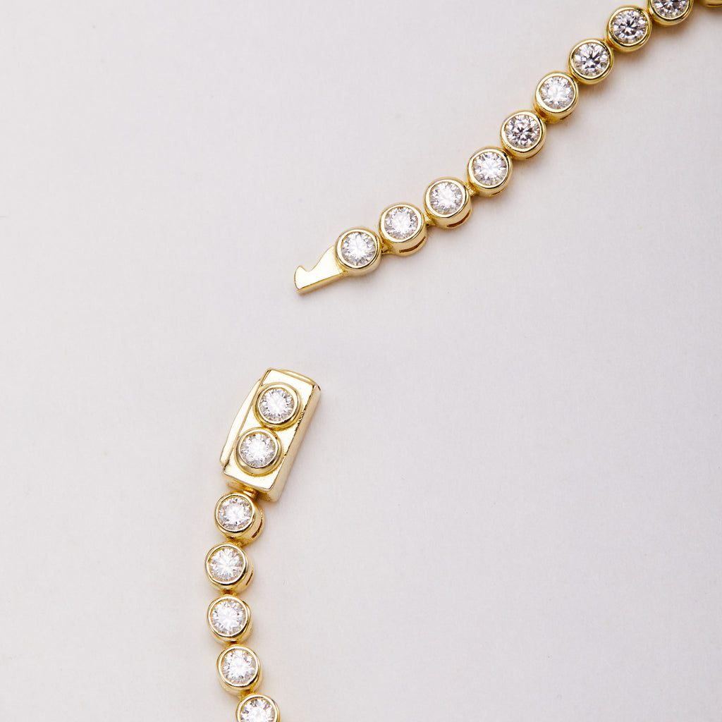 Close-up of an open gold-tone bracelet clasp with round clear stones, showing the clasp body and projecting tongue.