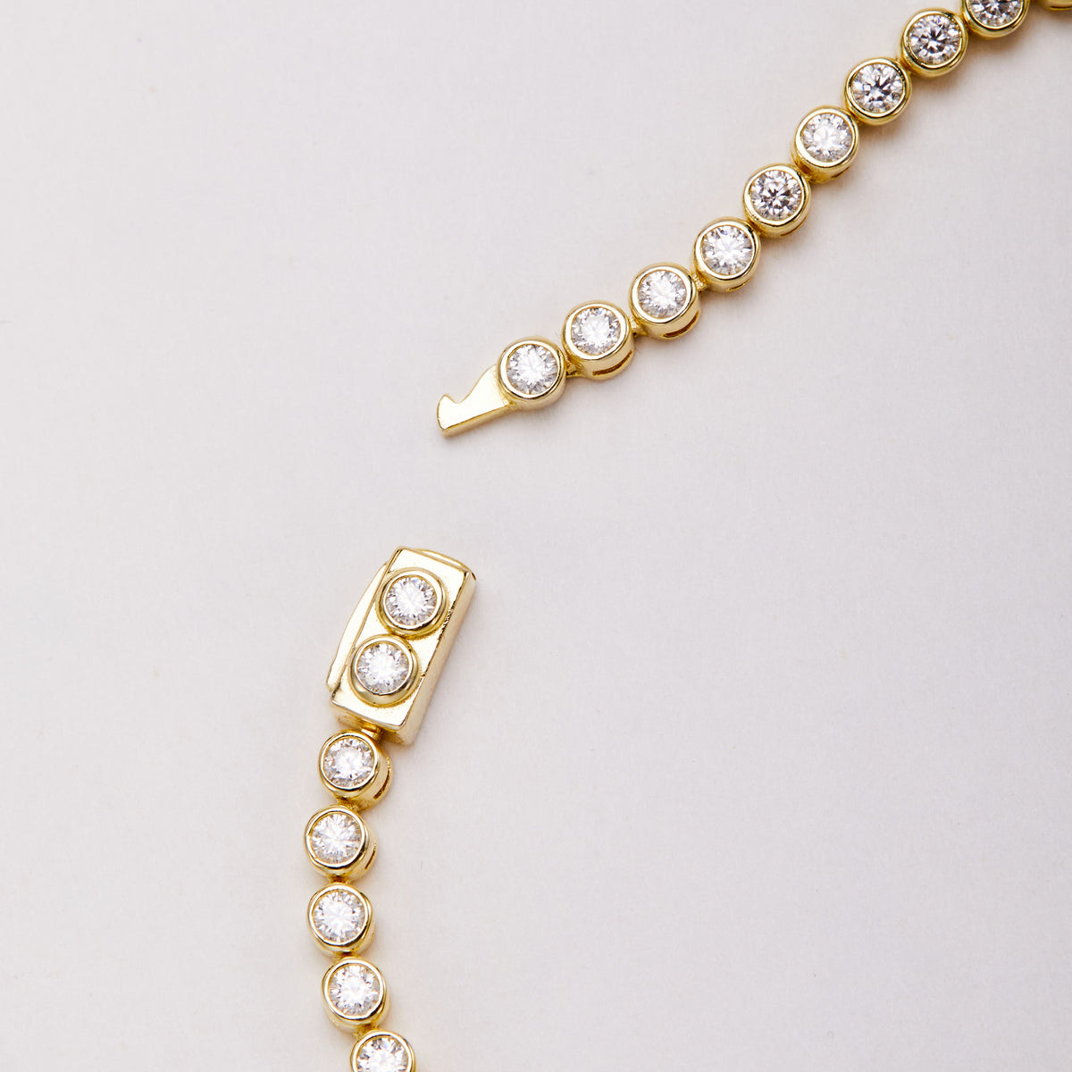 Close-up of an open gold-tone bracelet clasp with round clear stones, showing the clasp body and projecting tongue.
