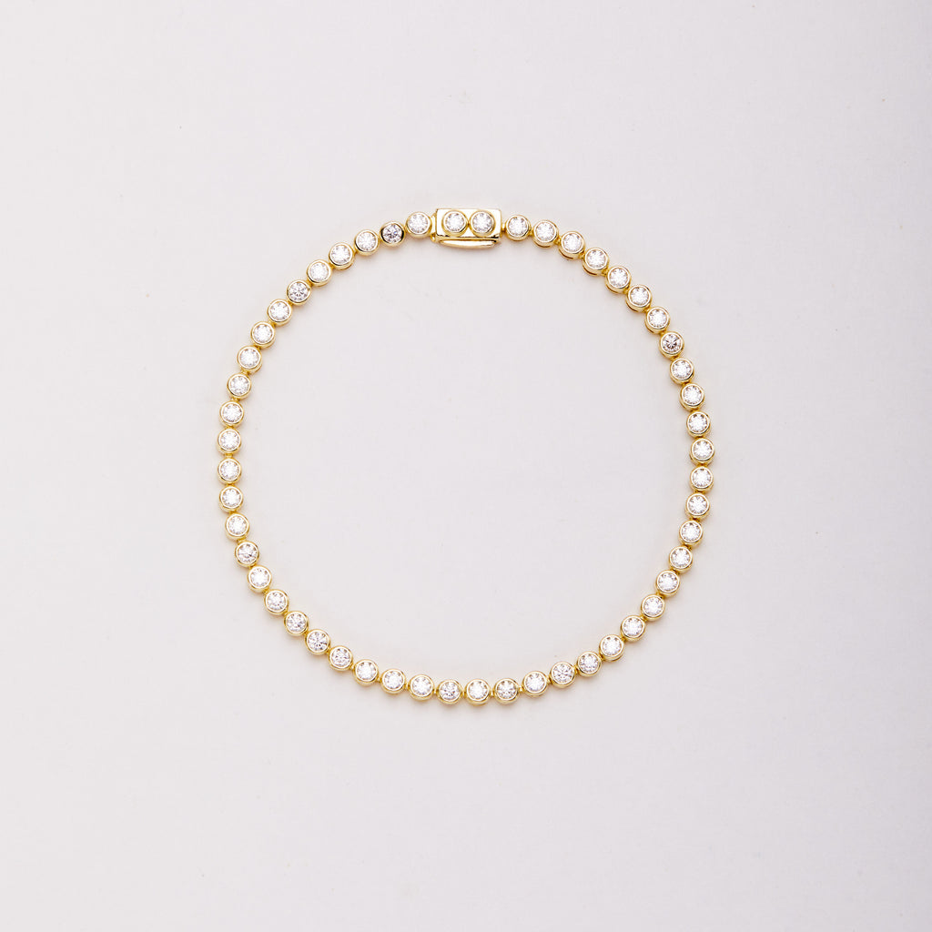 Gold-tone bracelet with round clear stones in bezel settings, laid flat in a closed loop with the clasp at the top.