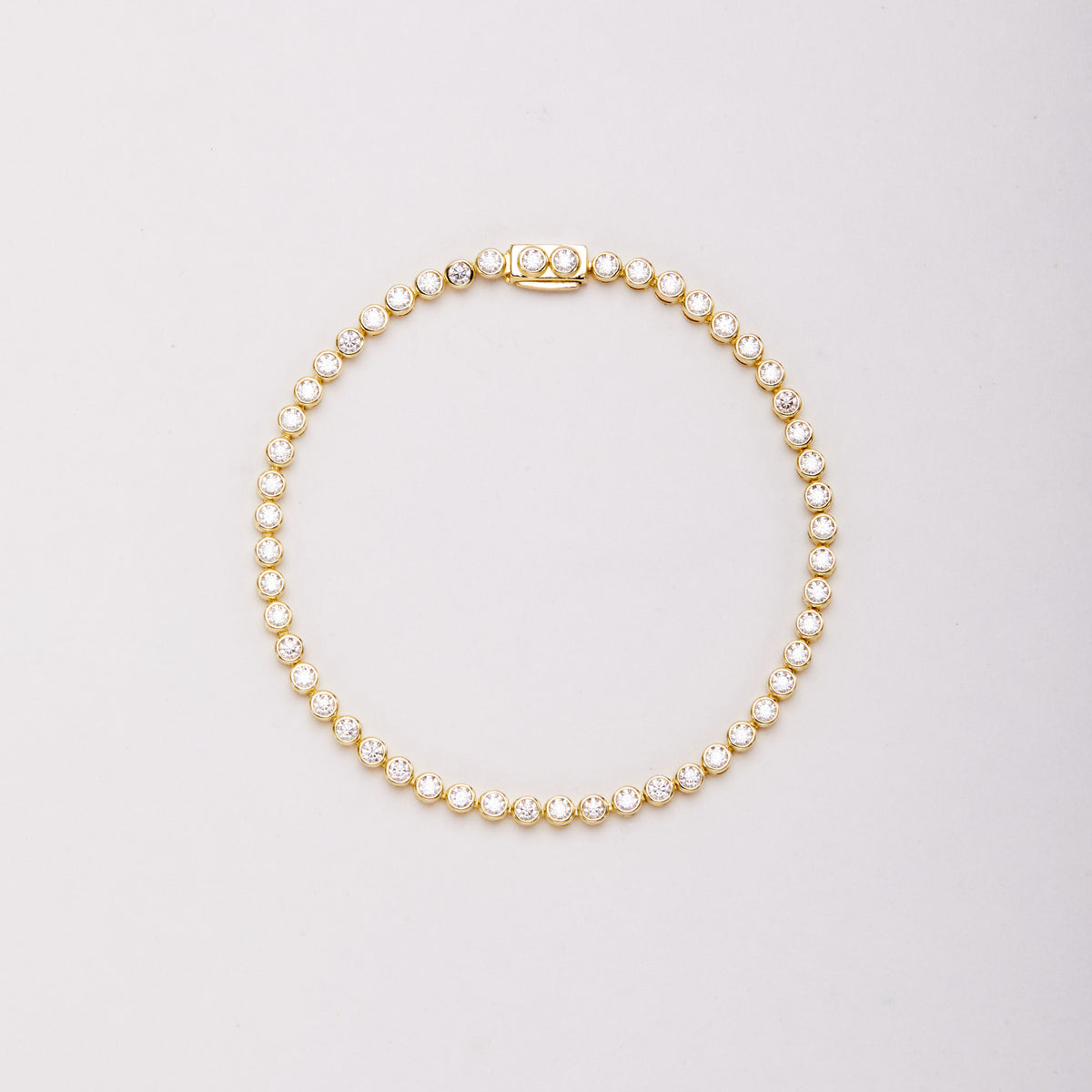 Gold-tone bracelet with round clear stones in bezel settings, laid flat in a closed loop with the clasp at the top.