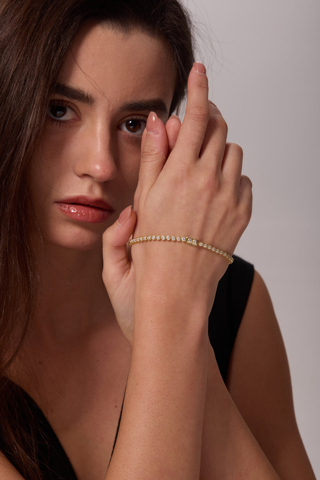 Gold-tone bracelet with round clear stones worn on a raised wrist in front of the face.