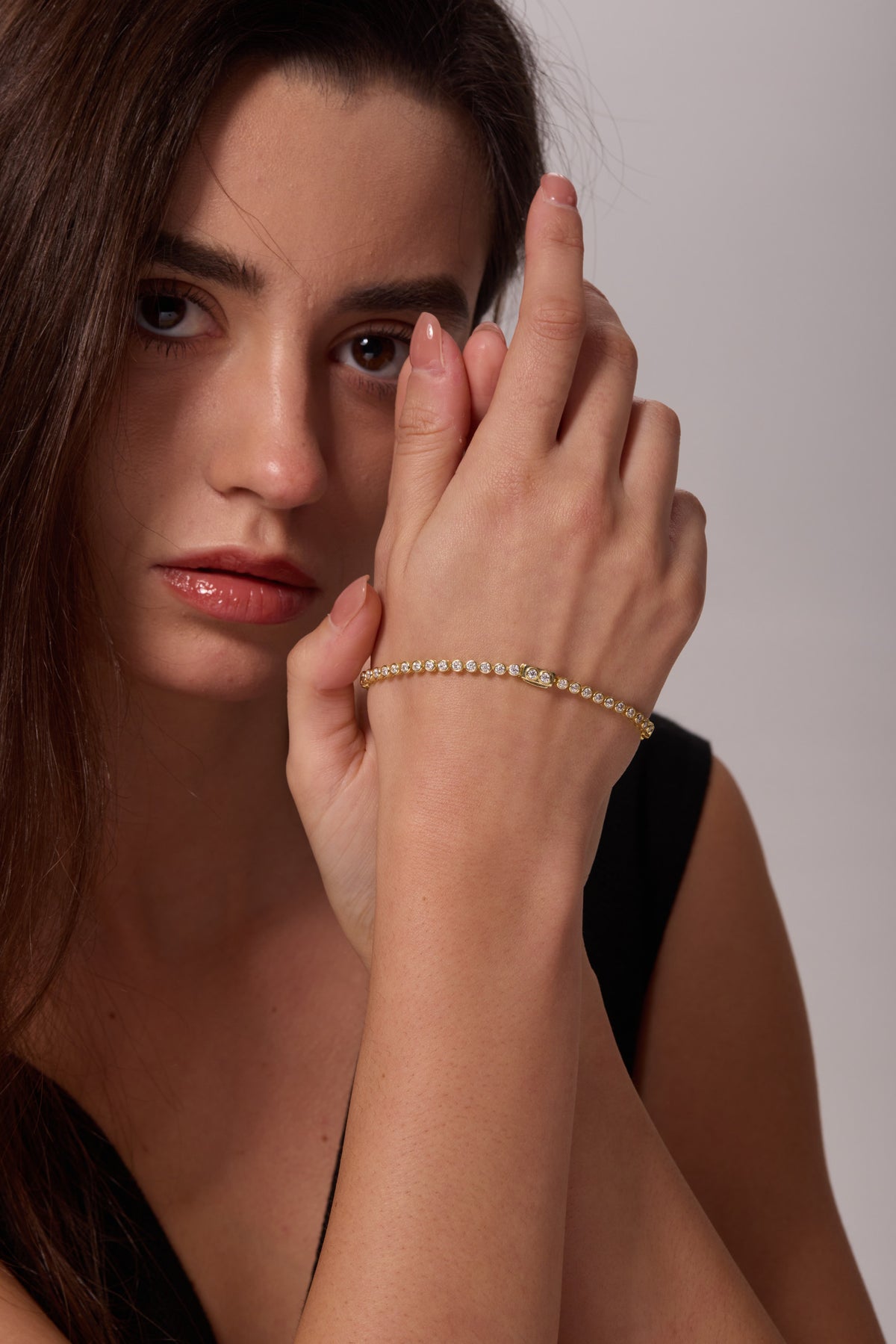 Gold-tone bracelet with round clear stones worn on a raised wrist in front of the face.
