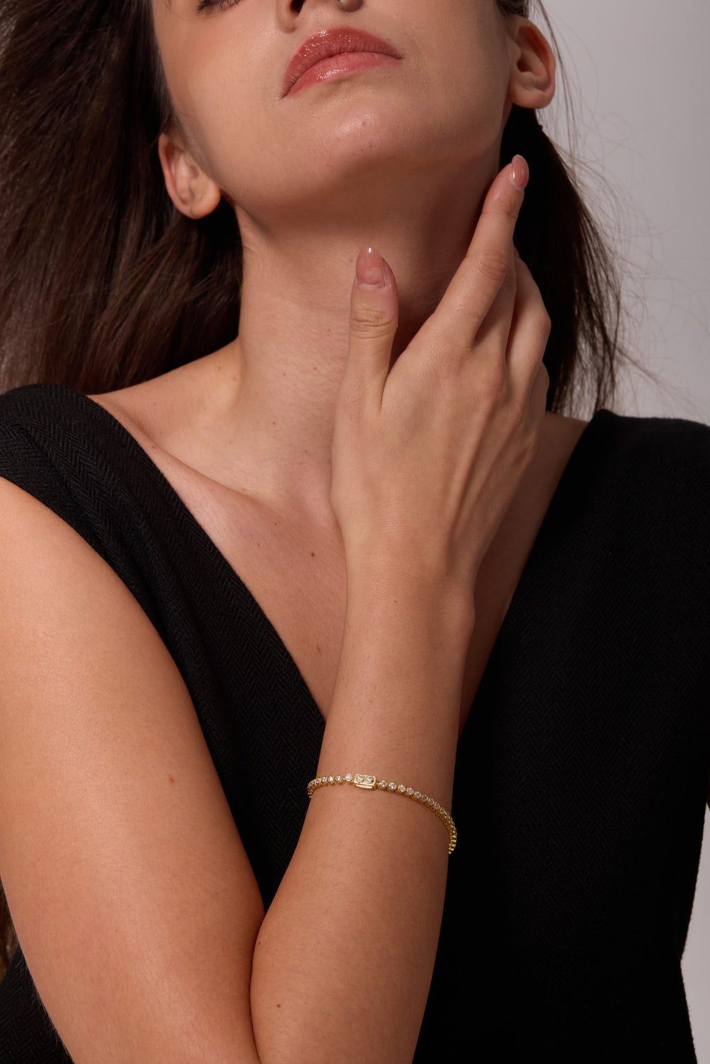 Gold-tone bracelet with round clear stones worn on a wrist beneath a hand resting against the neck.