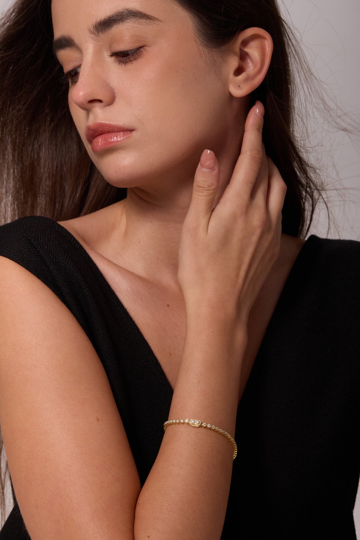 Gold-tone bracelet with round clear stones on a wrist, with the hand raised beside the neck.