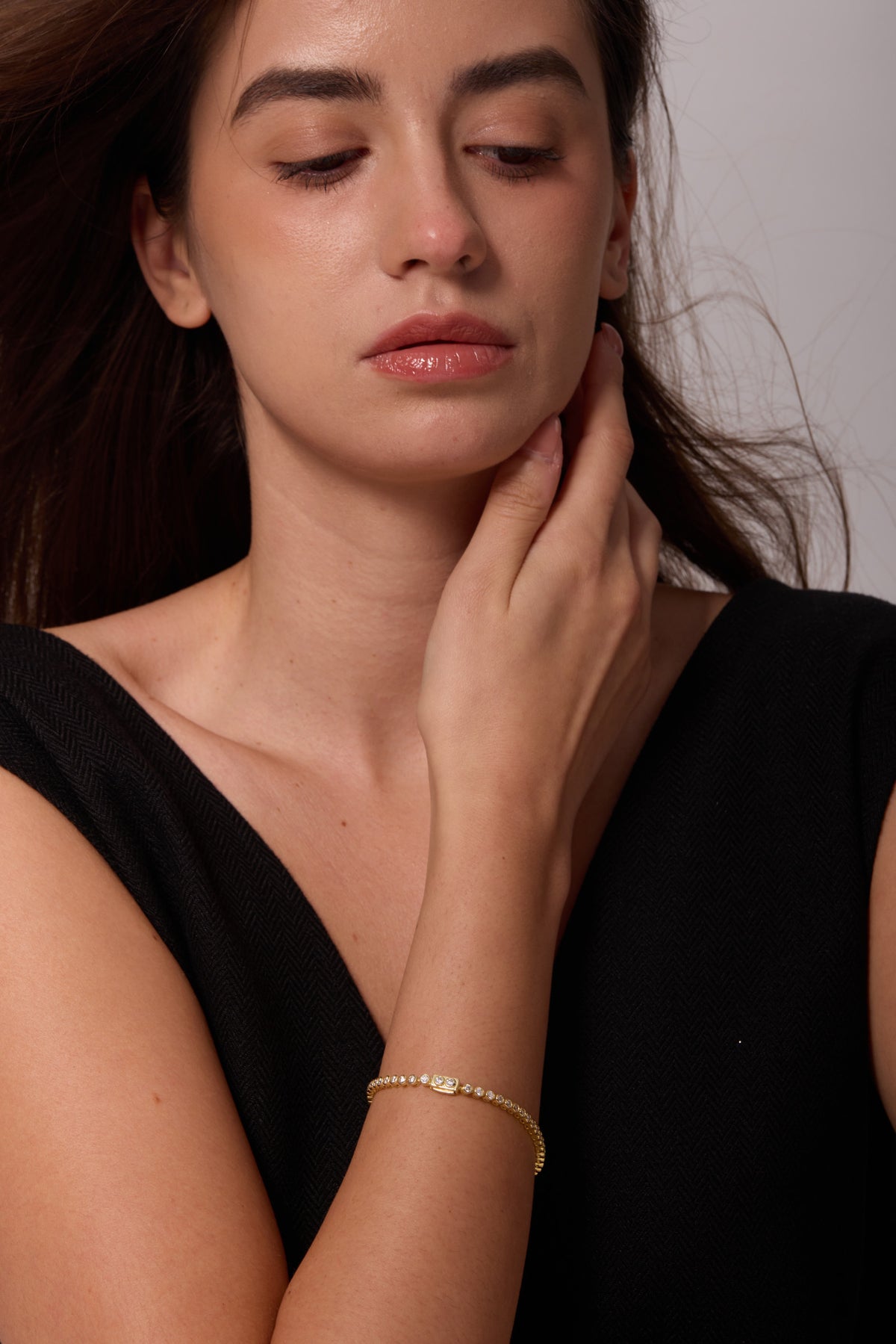 Gold-tone bracelet with round bezel-set stones, worn on a wrist as the hand rests at the neck.