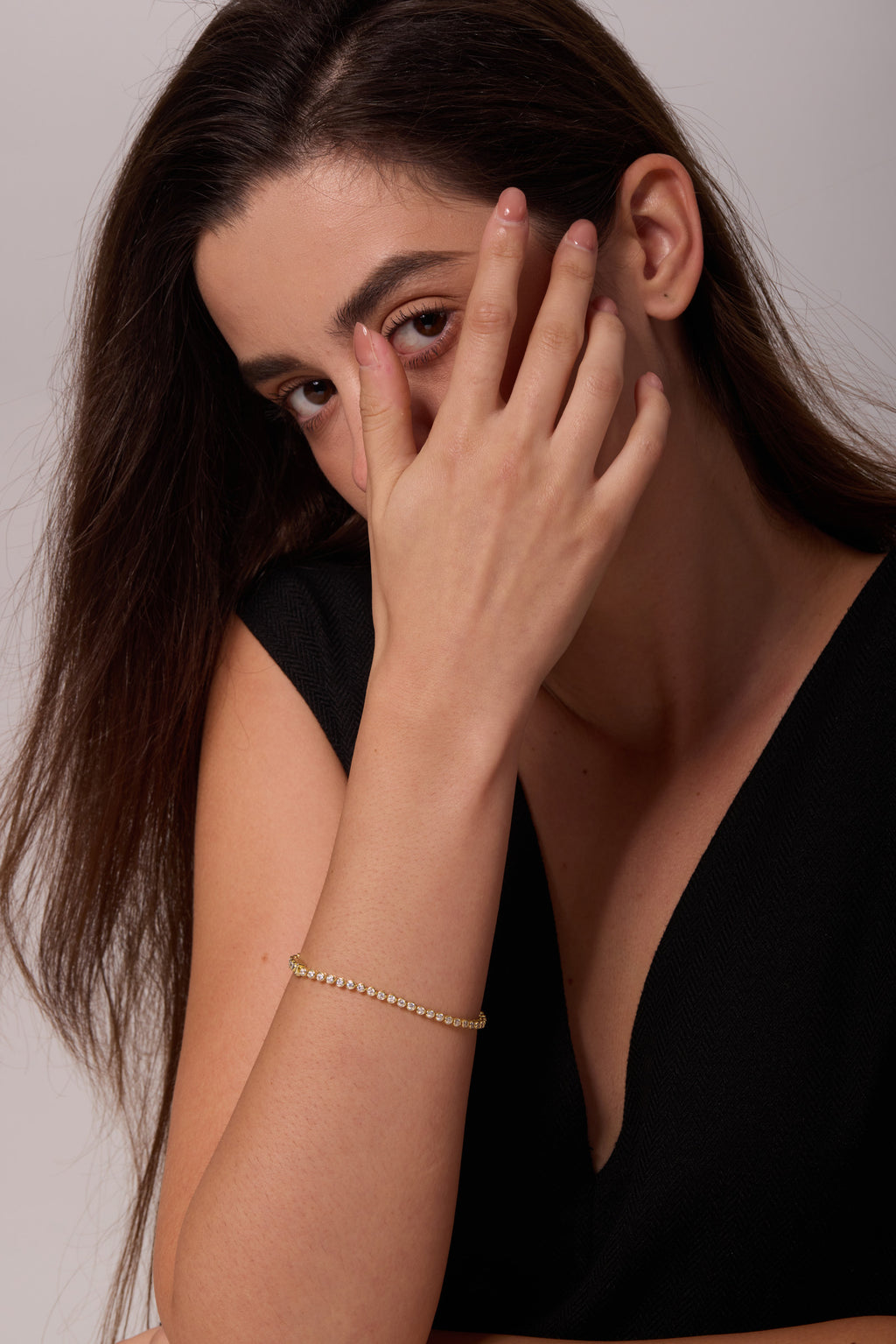 Gold-tone bracelet with round clear stones on a raised wrist, with the hand resting across the cheek.