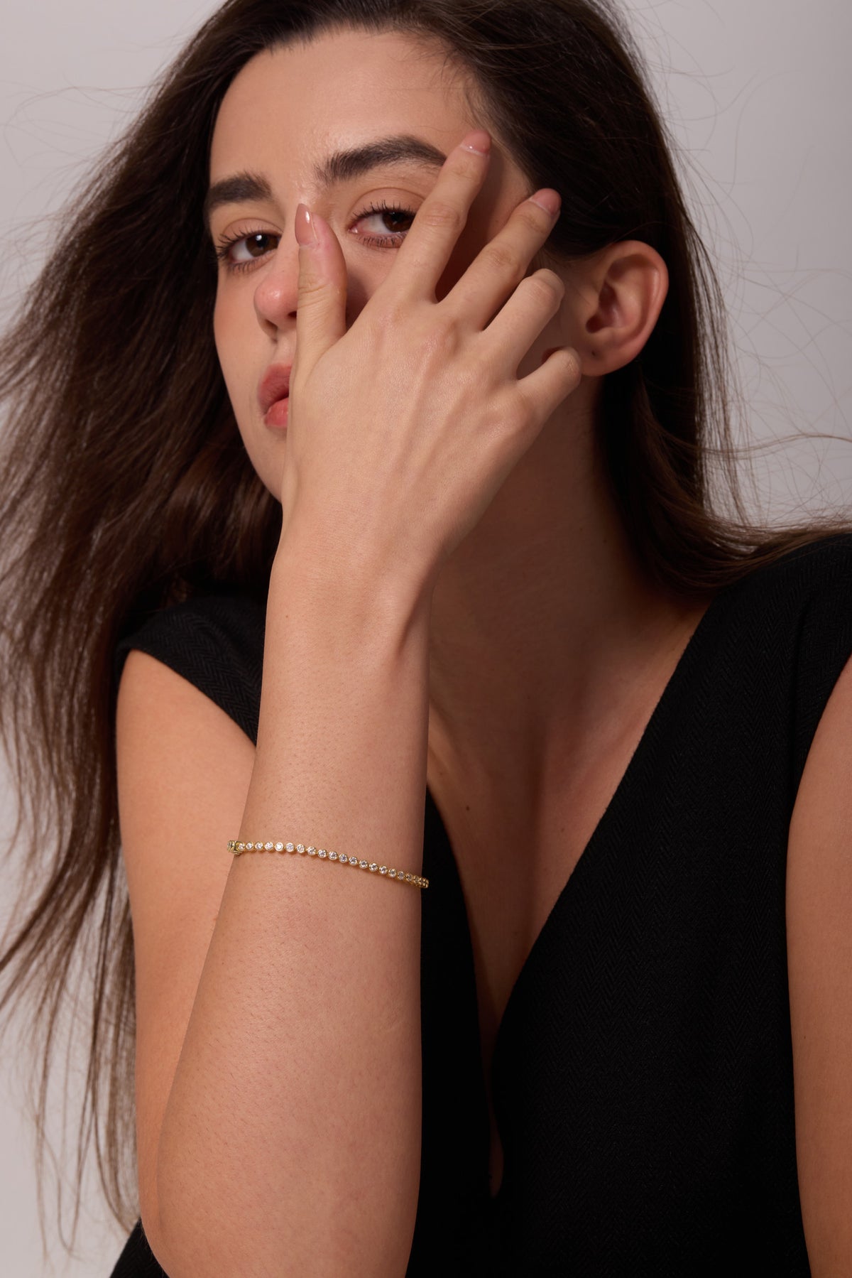 Gold-tone bracelet with round clear stones on an upright wrist, with the hand resting against the face.