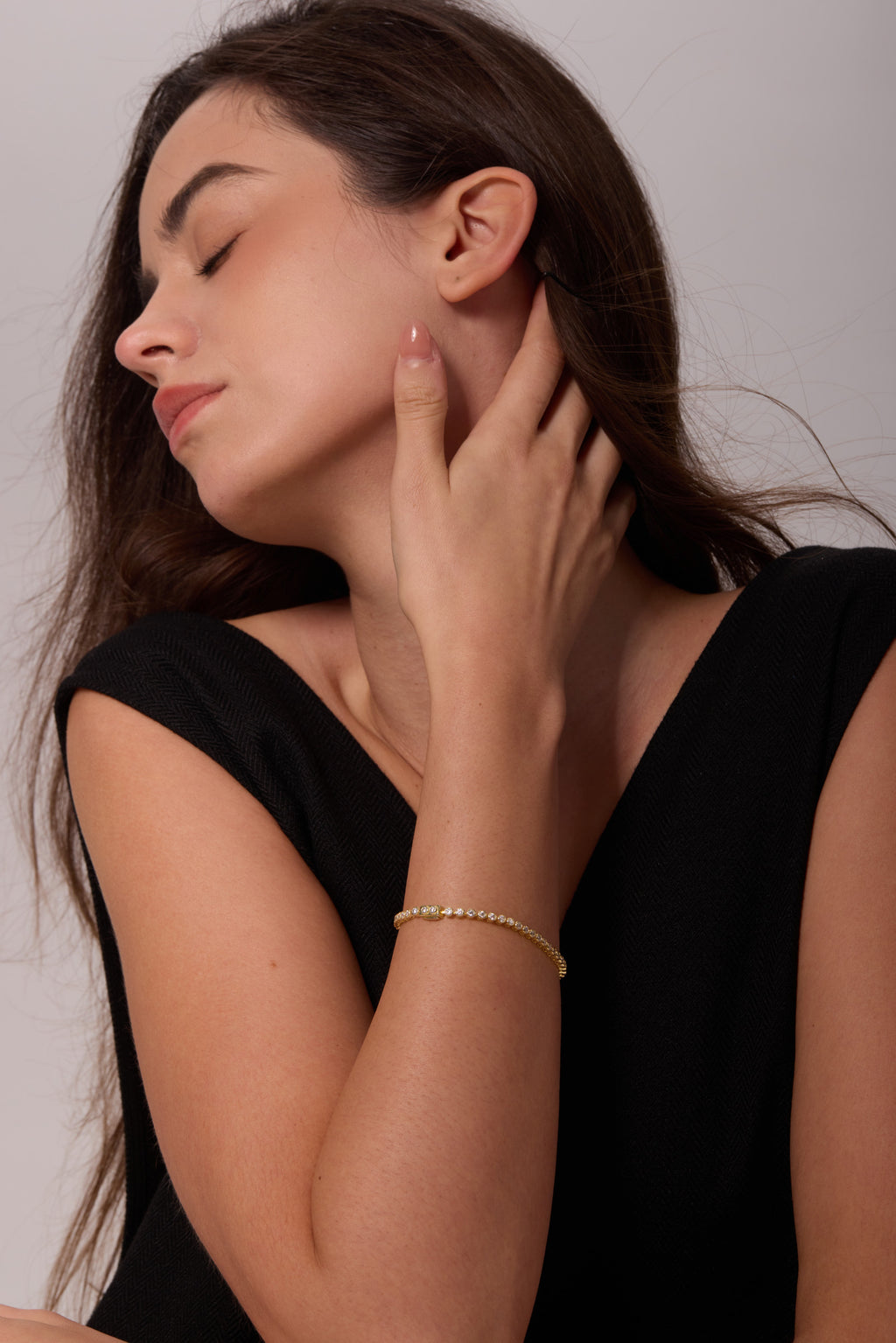 Side view of a gold-tone bracelet with round clear stones on a wrist, with the hand resting at the neck.