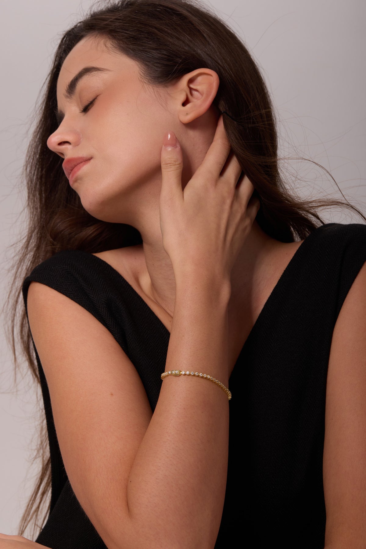 Side view of a gold-tone bracelet with round clear stones on a wrist, with the hand resting at the neck.