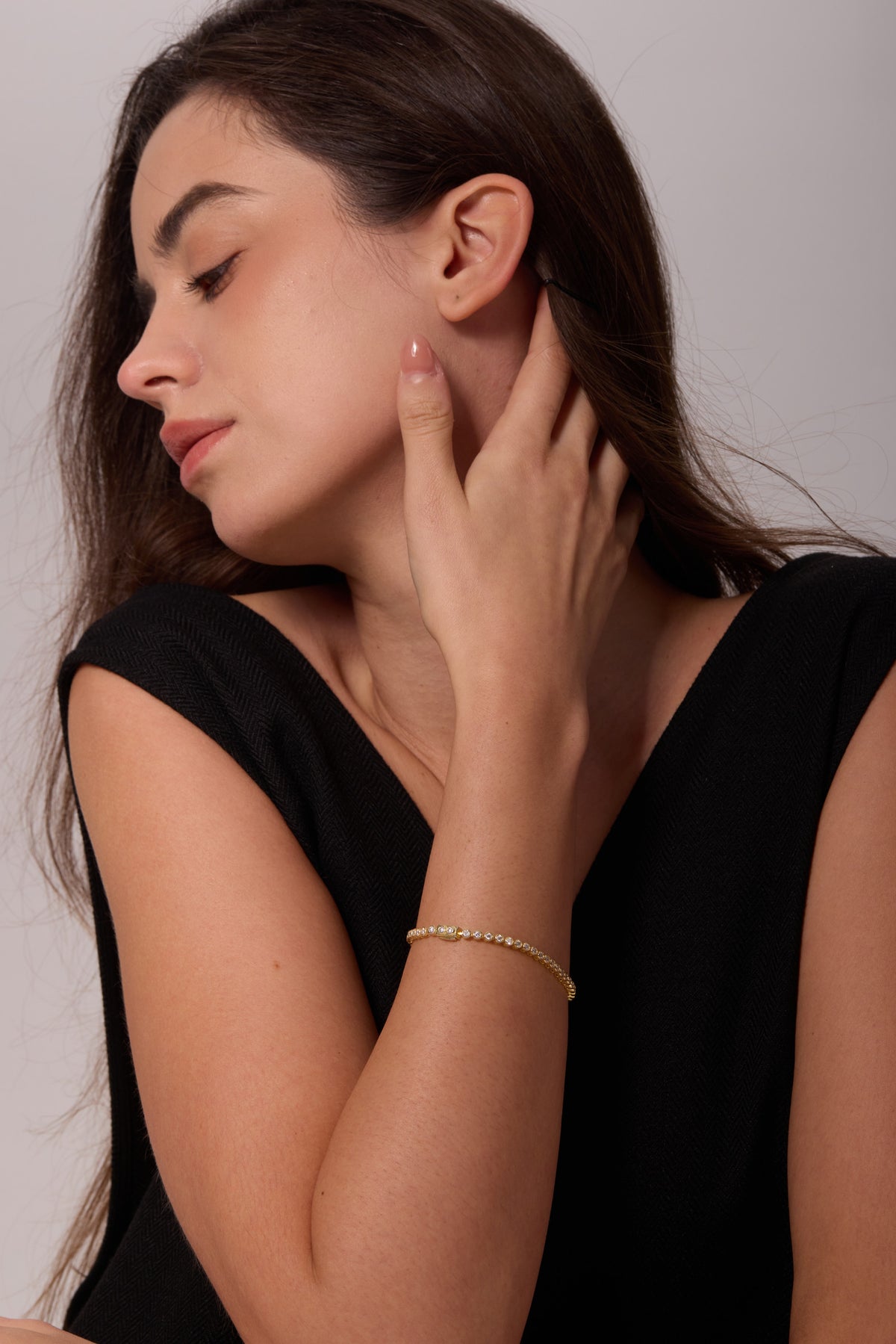 Gold-tone bracelet with round bezel-set stones, worn on a wrist with the hand beside the jaw.