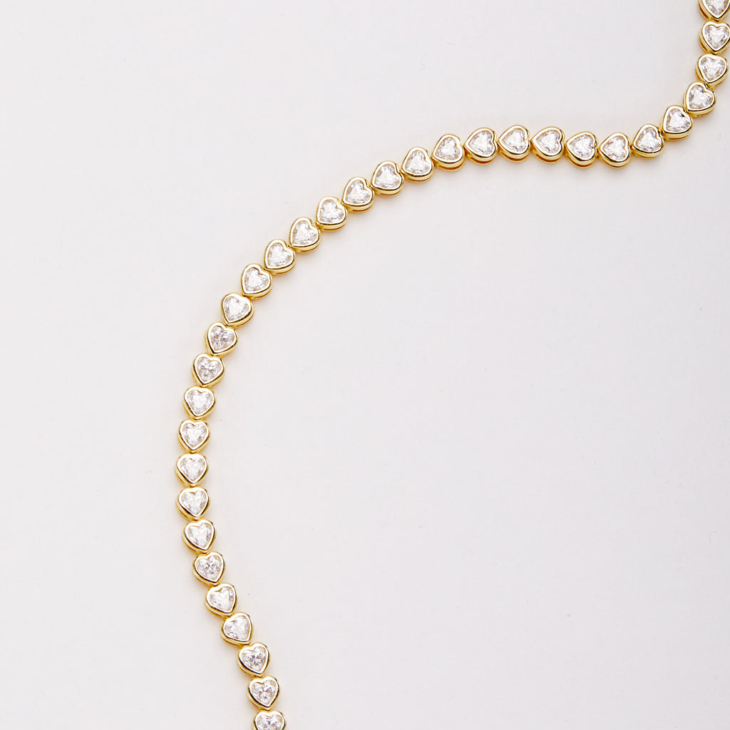 Close-up of a curved section of the bracelet with heart-shaped clear stones in gold-tone bezel settings.