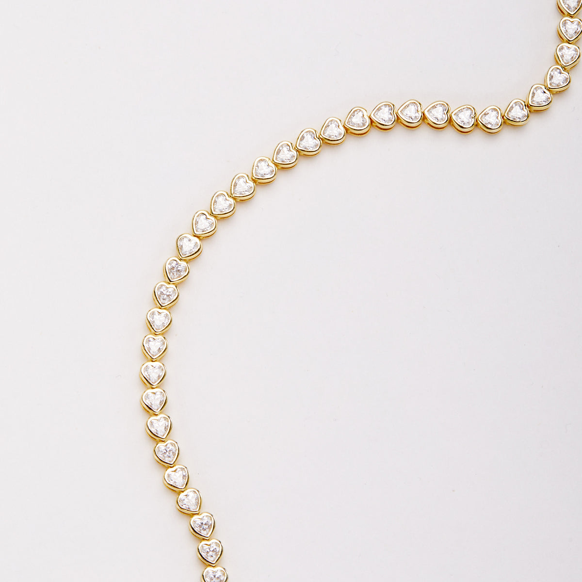 Close-up of a curved section of the bracelet with heart-shaped clear stones in gold-tone bezel settings.
