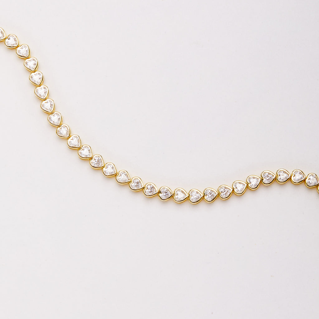 Close-up of the bracelet laid in a broad curve, showing heart-shaped clear stones in gold-tone bezel settings.