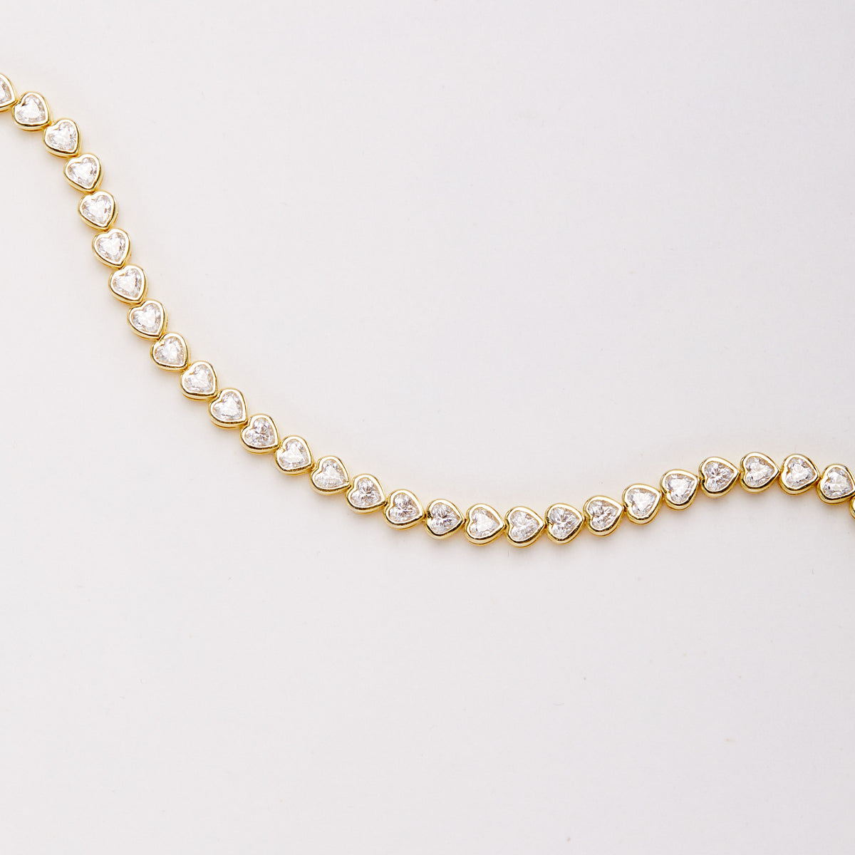 Close-up of the bracelet laid in a broad curve, showing heart-shaped clear stones in gold-tone bezel settings.