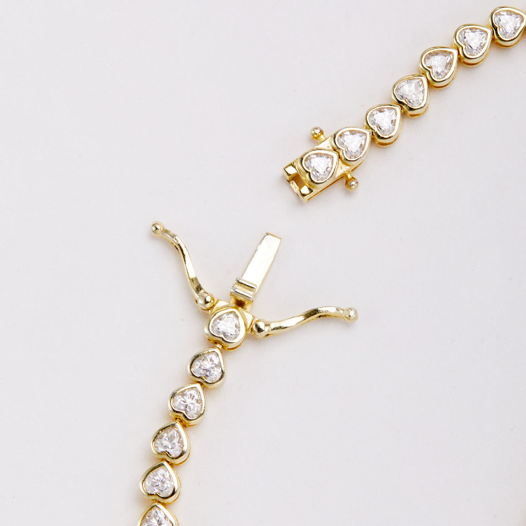 Close-up of the open clasp on a gold-tone bracelet with heart-shaped clear stones, showing the tongue and two safety arms.