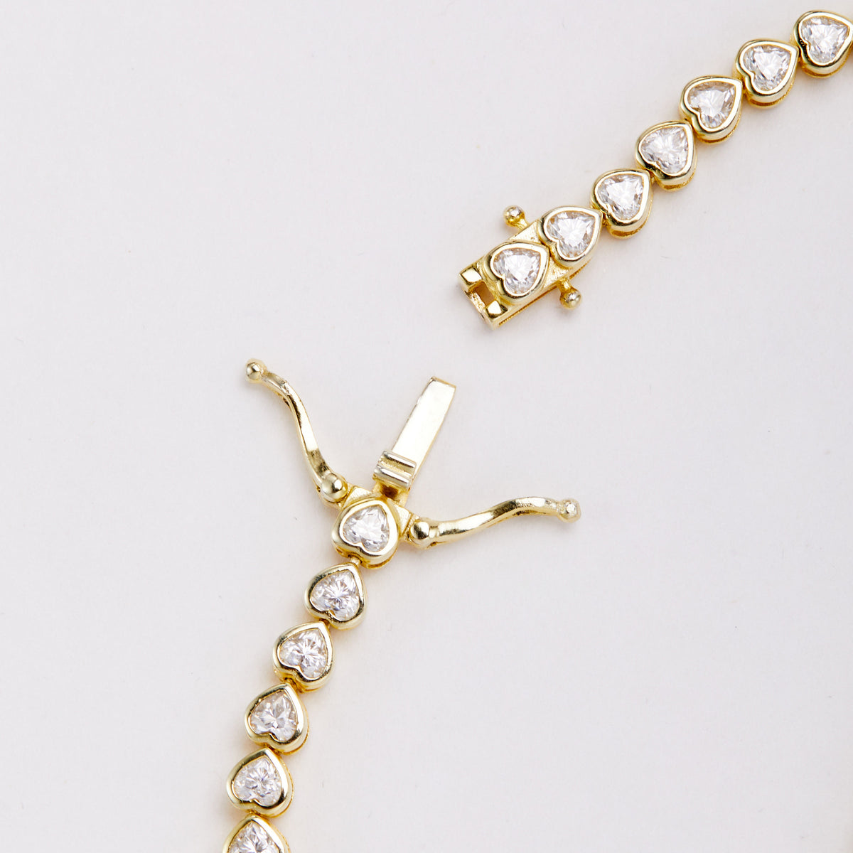 Close-up of the open clasp on a gold-tone bracelet with heart-shaped clear stones, showing the tongue and two safety arms.