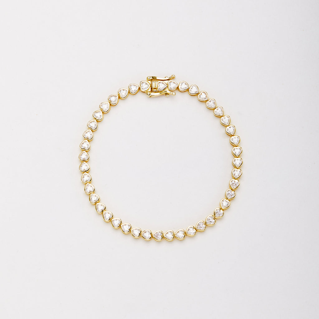 Gold-tone bracelet with heart-shaped clear stones in bezel settings, laid flat in a closed loop with the clasp at the top.