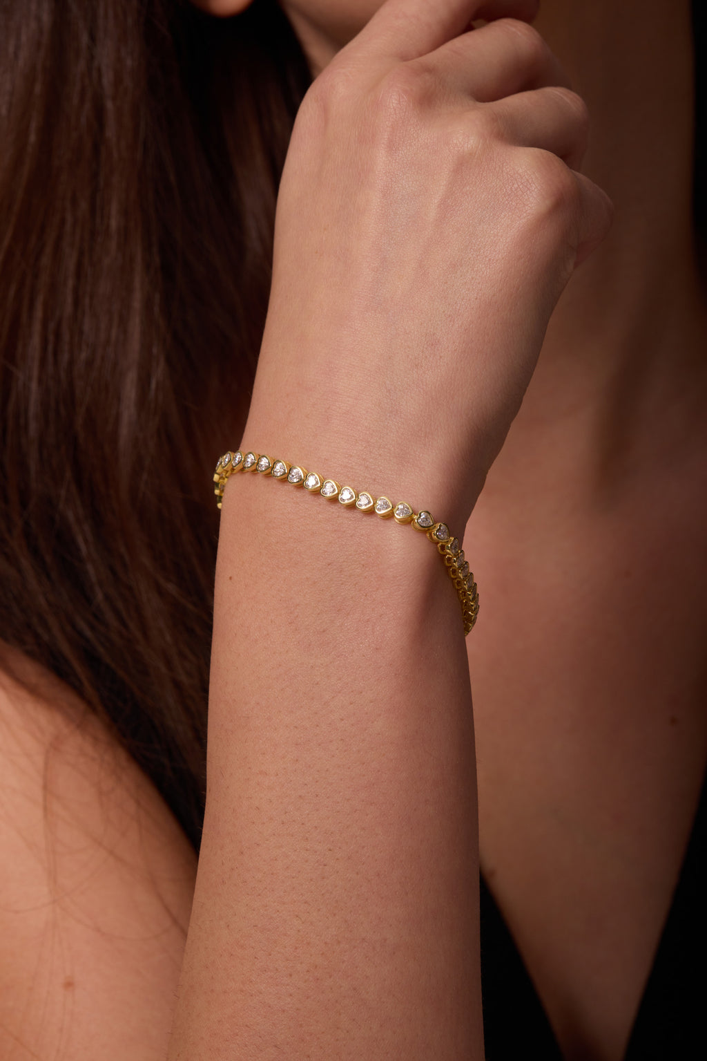 Gold-tone bracelet with heart-shaped clear stones, shown close up on a raised wrist.