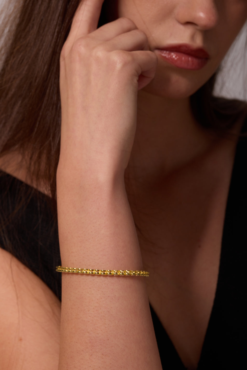 Side view of a gold-tone linked bracelet on a raised wrist, with the hand beside the cheek.