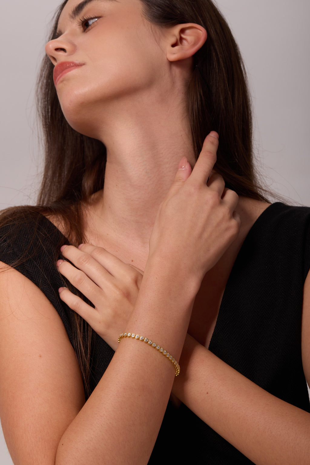 Gold-tone bracelet with clear stones, worn on a wrist across the chest with the hand beside the neck.