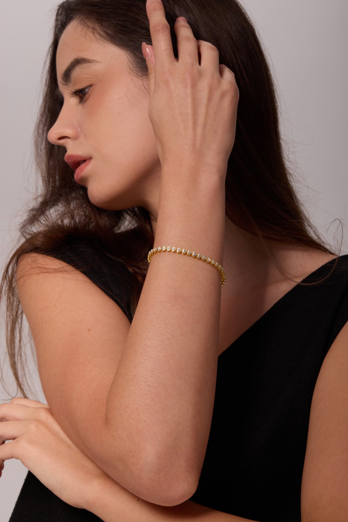 Gold-tone bracelet with heart-shaped clear stones, worn on a raised wrist with the hand in the hair.