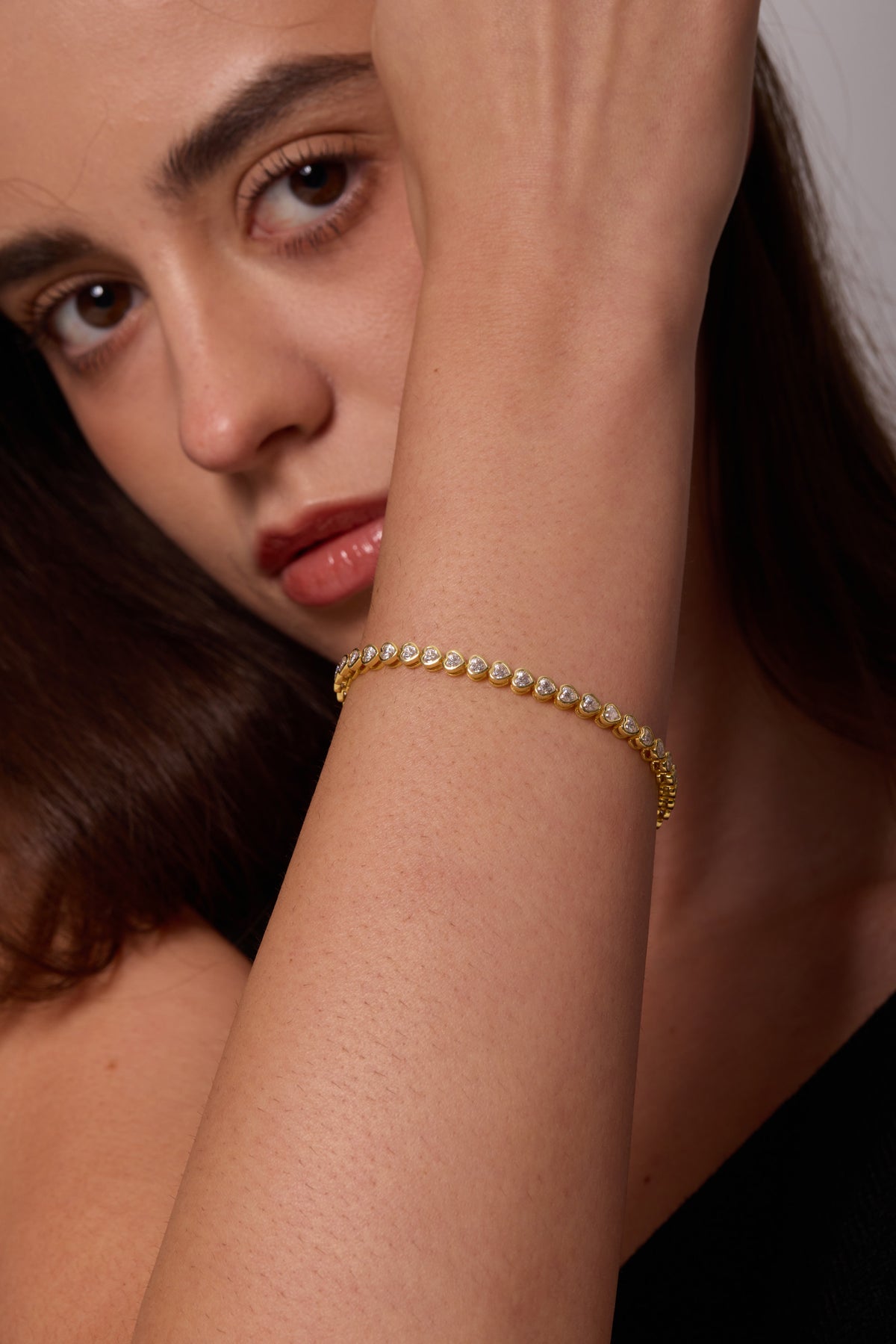 Close-up of a gold-tone bracelet with heart-shaped clear stones on a wrist raised in front of the face.