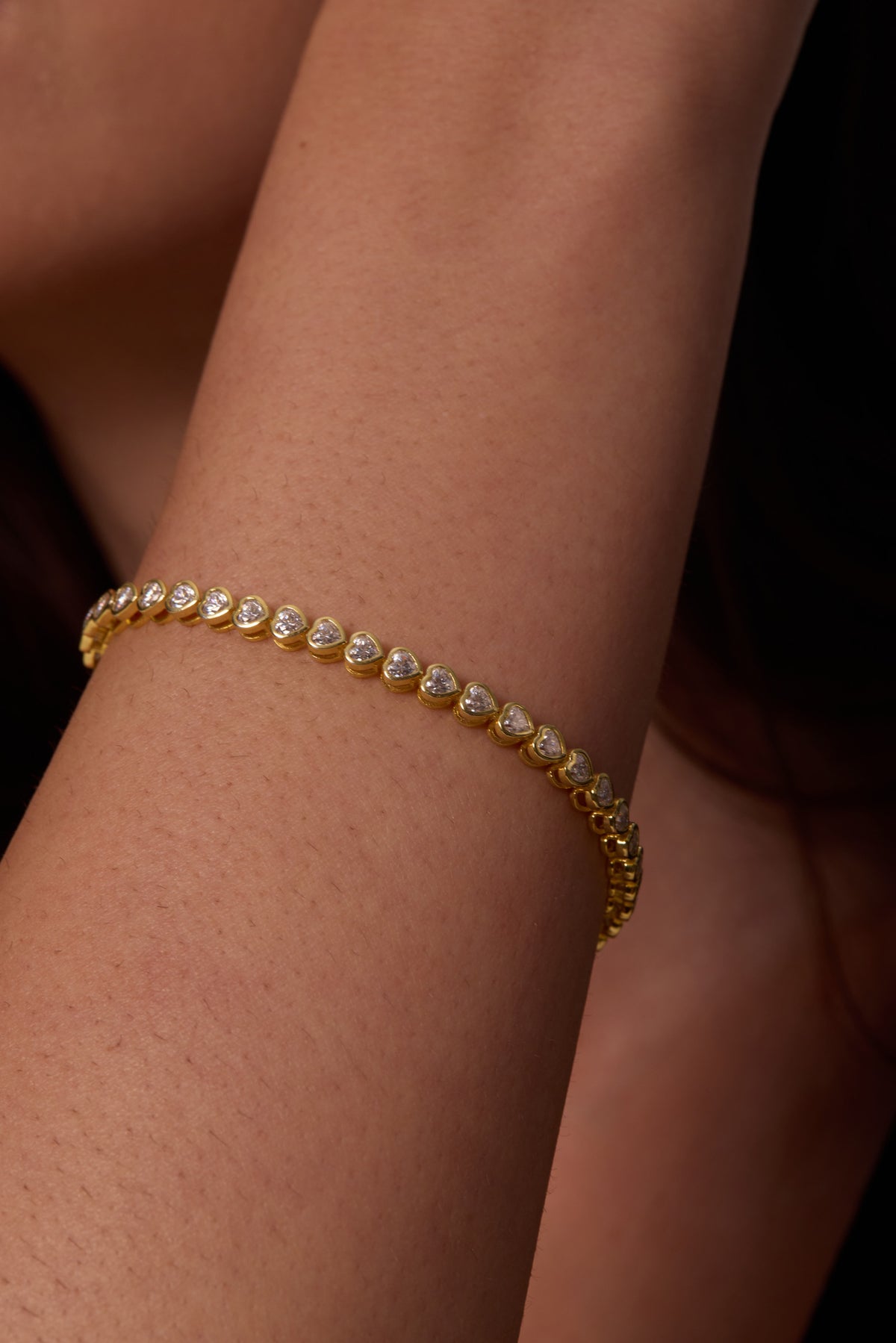 Close-up of a gold-tone bracelet with heart-shaped clear stones and linked settings around the wrist.