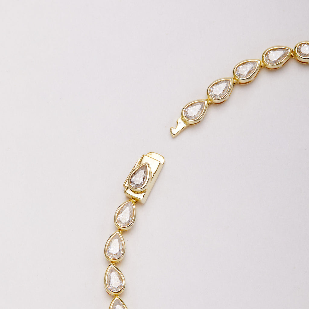 Close-up of the open clasp and pear-shaped bezel-set stones on a gold-tone bracelet.
