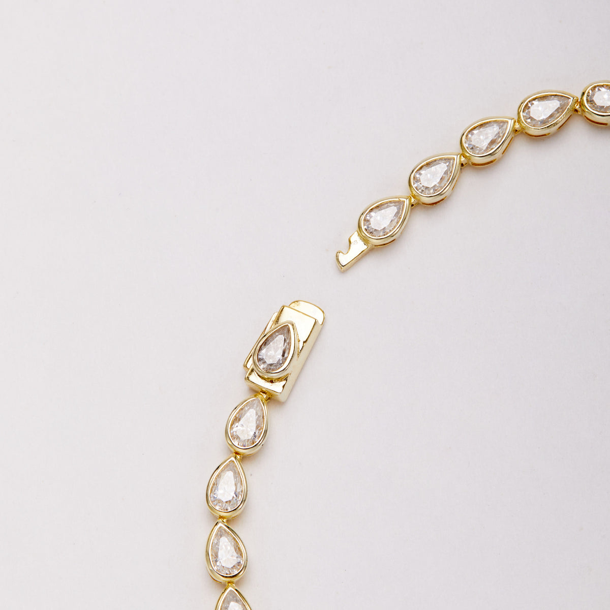 Close-up of the open clasp and pear-shaped bezel-set stones on a gold-tone bracelet.