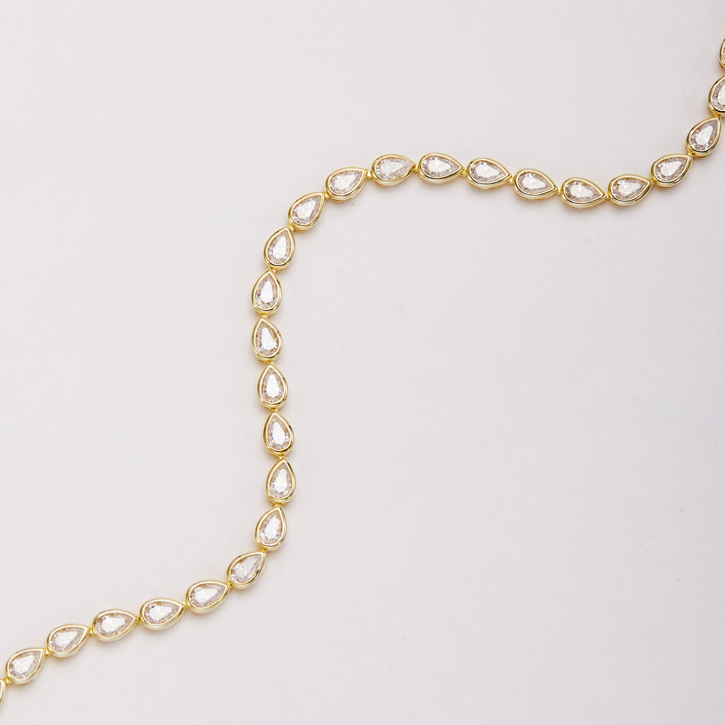 Close-up of a curved row of pear-shaped bezel-set stones linked in a gold-tone bracelet.