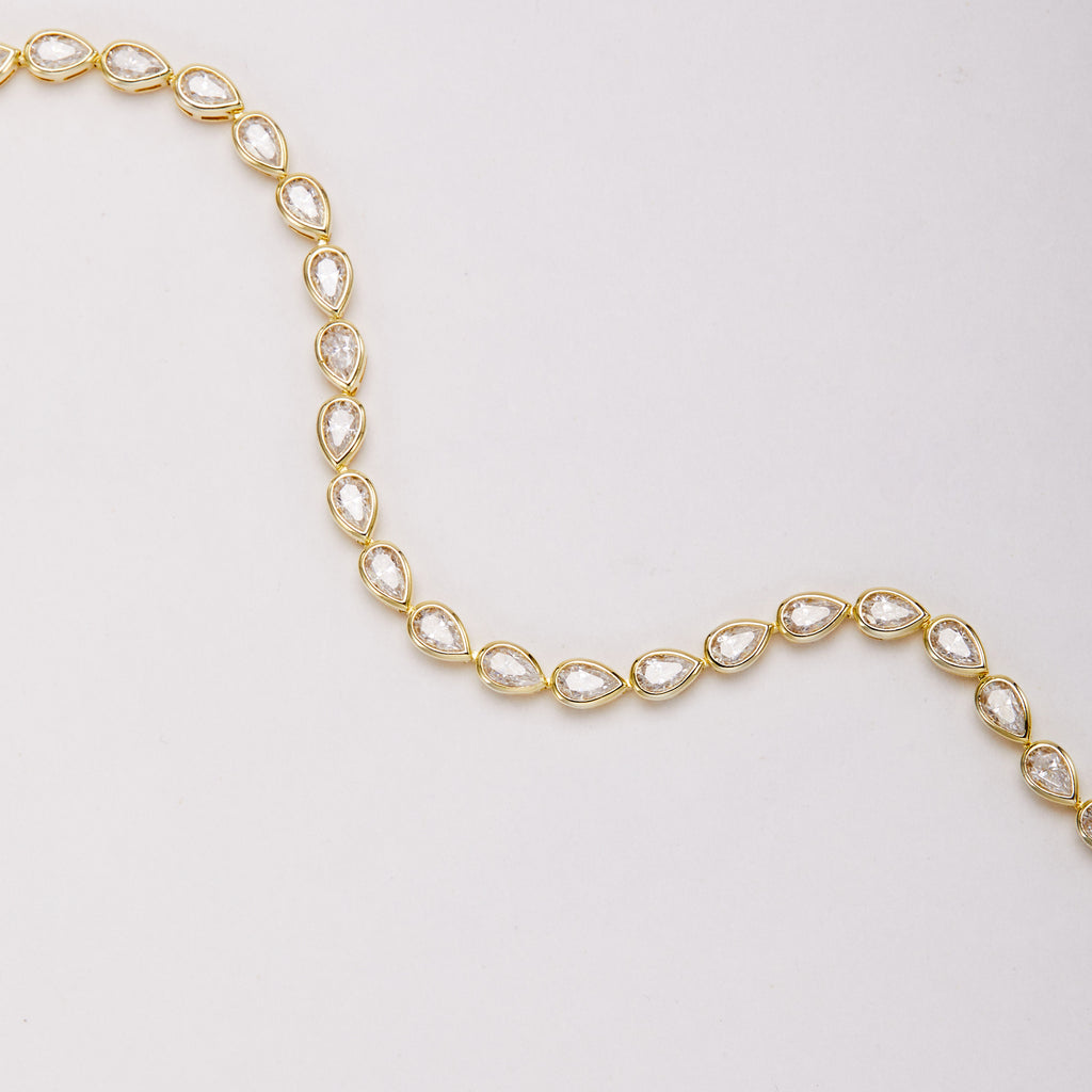 Close-up of a gold-tone bracelet arranged in a wave, showing pear-shaped bezel-set stones and connecting links.