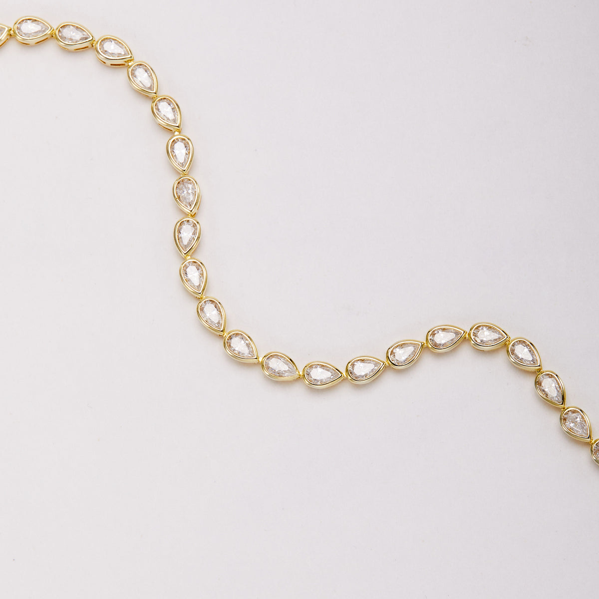 Close-up of a gold-tone bracelet arranged in a wave, showing pear-shaped bezel-set stones and connecting links.