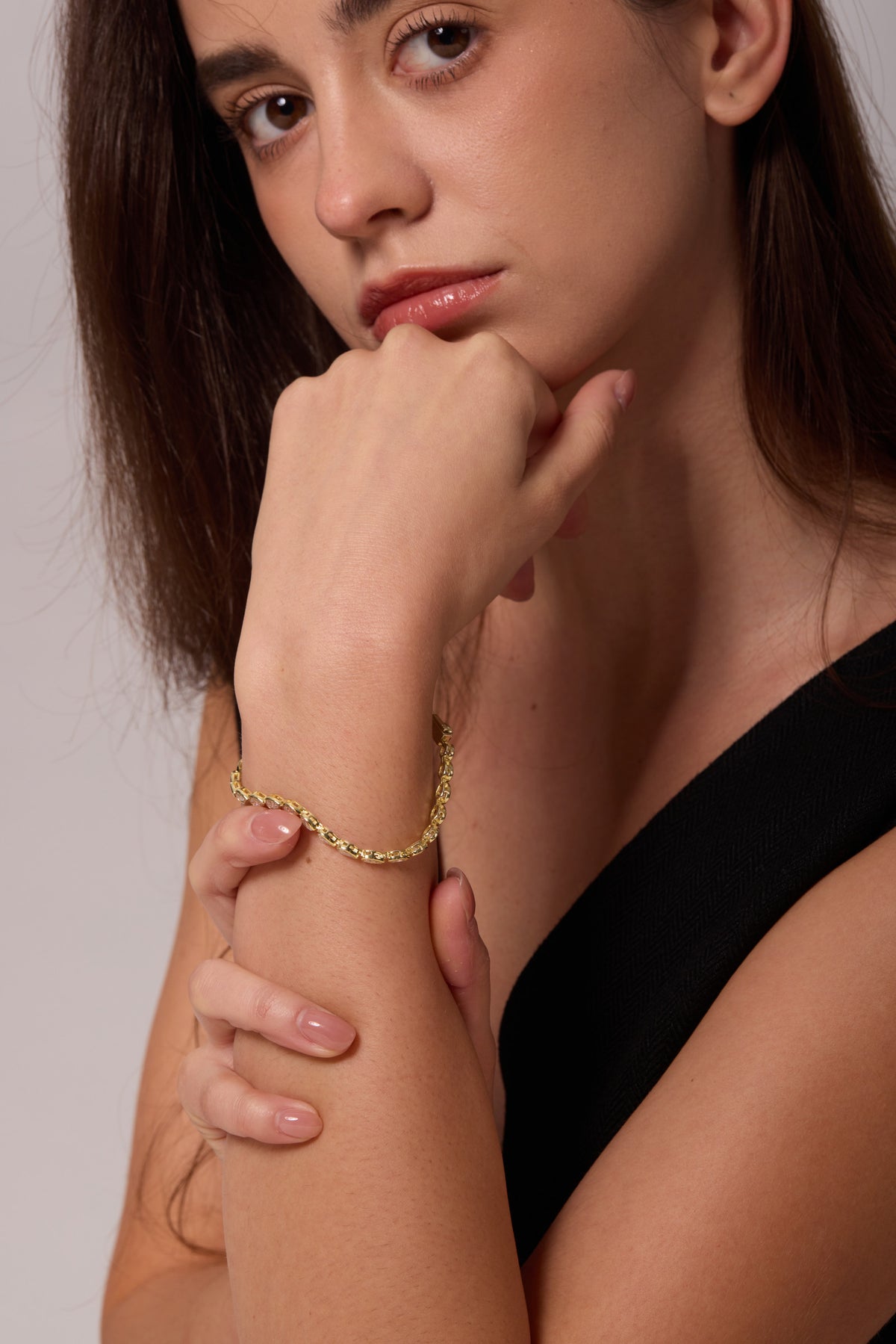 Side view of a gold-tone linked bracelet on a raised wrist held below the chin.