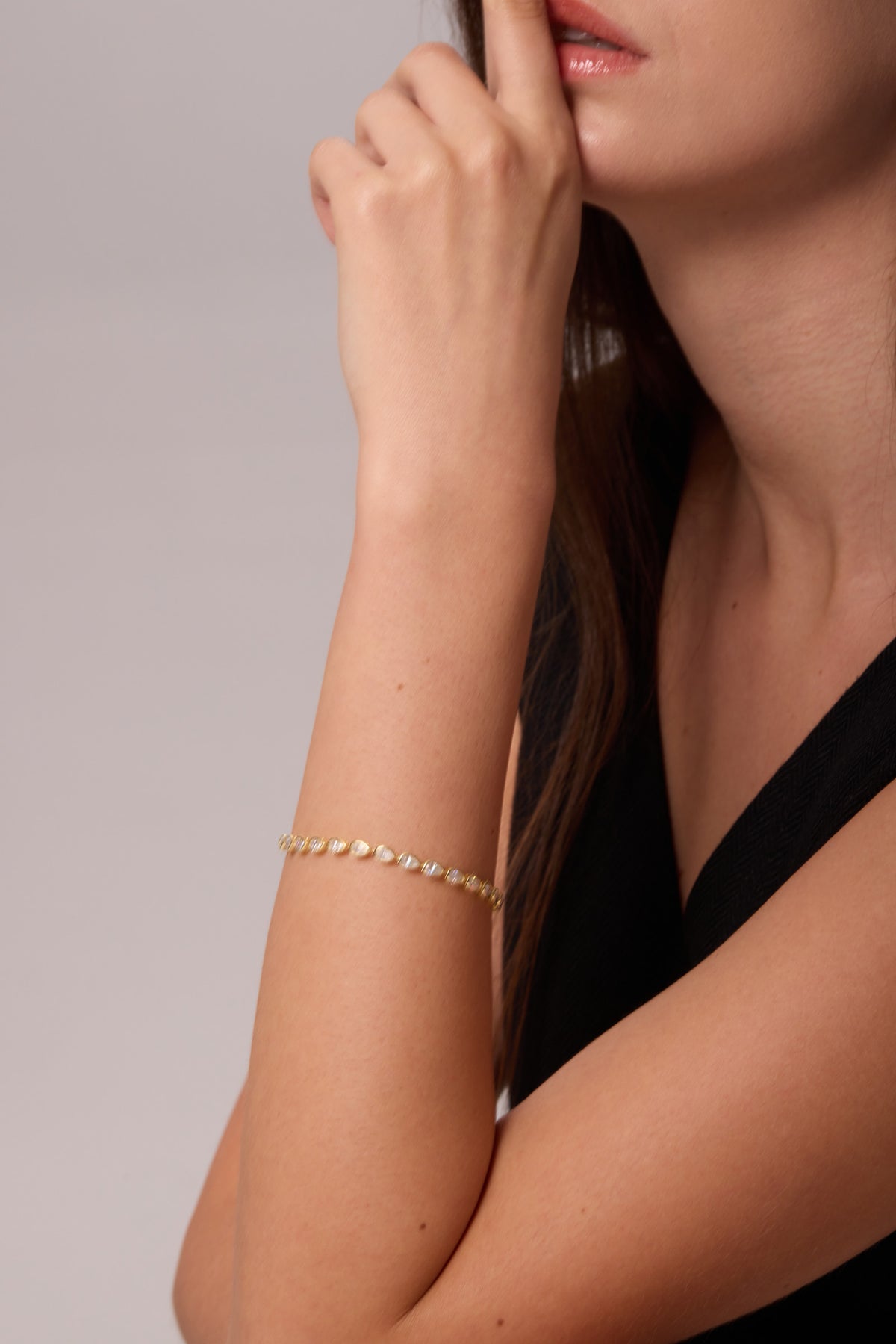 Gold-tone bracelet with a row of clear stones, worn on a raised wrist beside the face.