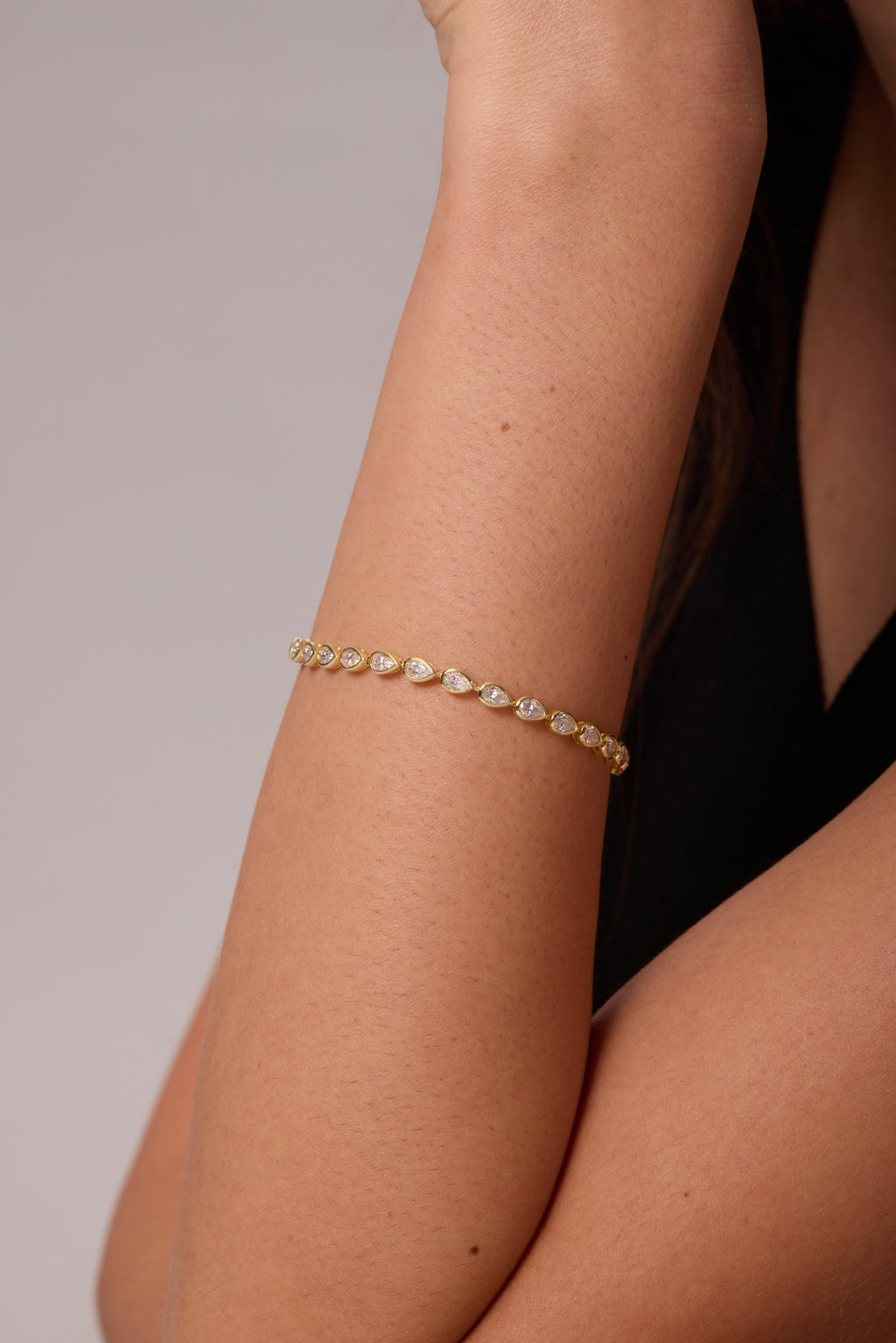 Close-up of pear-shaped clear stones in gold-tone bracelet settings around a raised wrist.