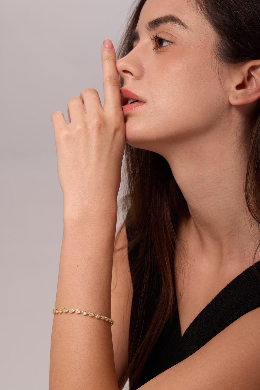 Gold-tone bracelet with pear-shaped clear stones on a raised wrist, shown beside the face in profile.