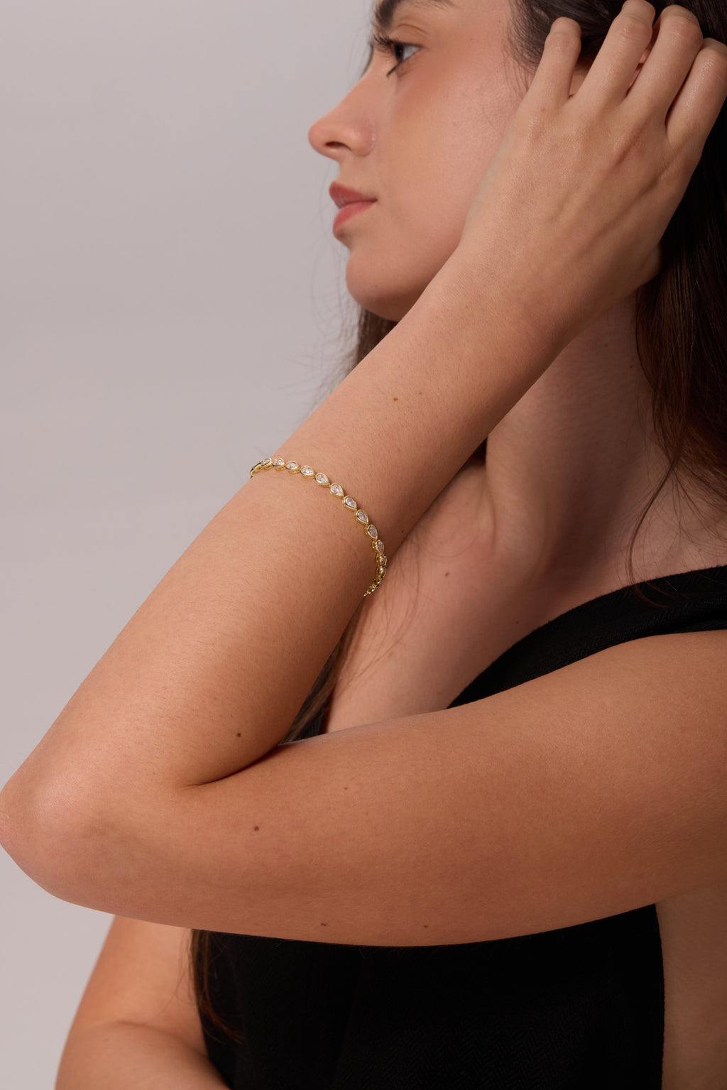 Gold-tone bracelet with pear-shaped clear stones, worn on a bent wrist with the hand touching the hair.